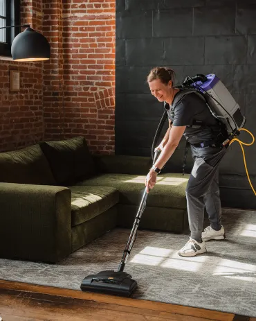 Merry Maids of Lancaster County professional cleaner using a backpack vacuum on a living room rug.