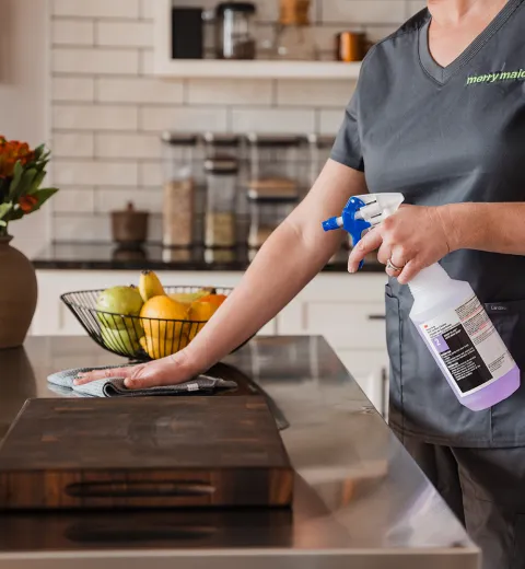 Merry Maids of Berks County professional house cleaner wiping down a kitchen countertop with a microfiber cloth and all-purpose cleaning spray